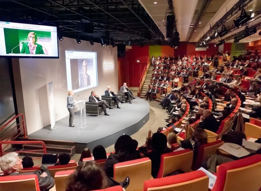 Auditorium en configuration plénière : intervenants sur scène face à un public assis en gradins